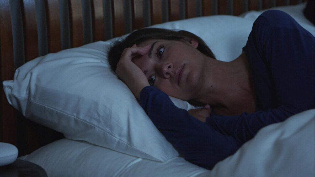 A woman in bed looking stressed because noise is keeping her awake.