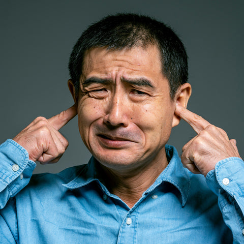 Older Asian Man with fingers in his ears to not hear noise