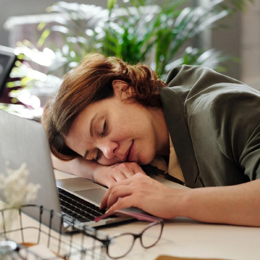 A woman asleep at her desk during her workday, hands on laptop keyboard