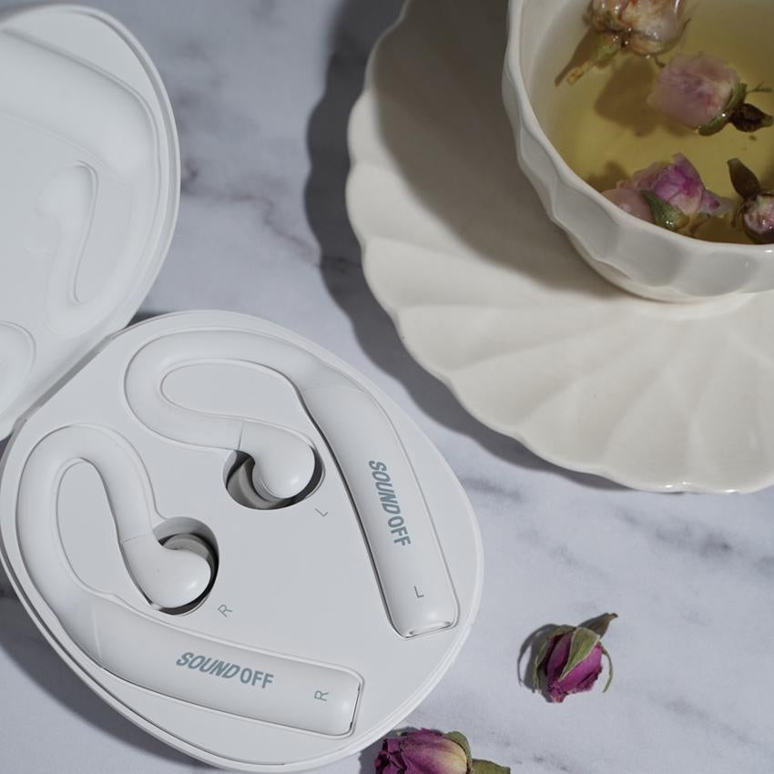 SoundOff sleep earbuds lying in their charging case next to a cup of herbal tea, on a marble top table.