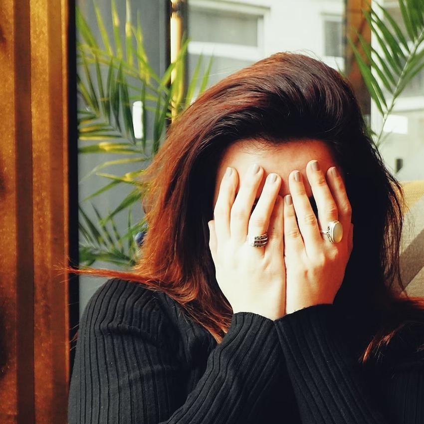 A stressed-out woman covers her face with both hands. Stress is one of the key reasons we can't fall asleep.