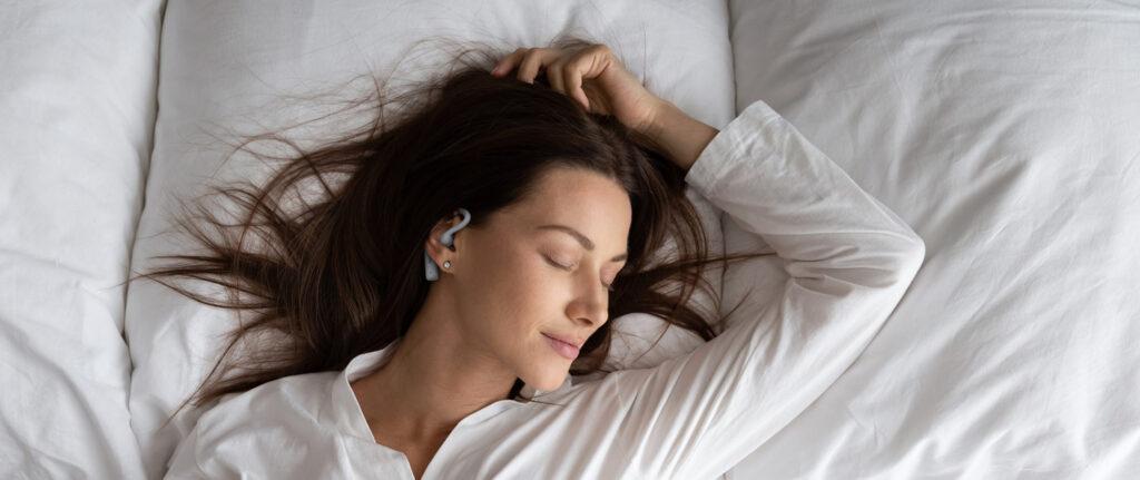 Woman sleeping peacefully in white bed wearing SoundOff noise masking earbuds