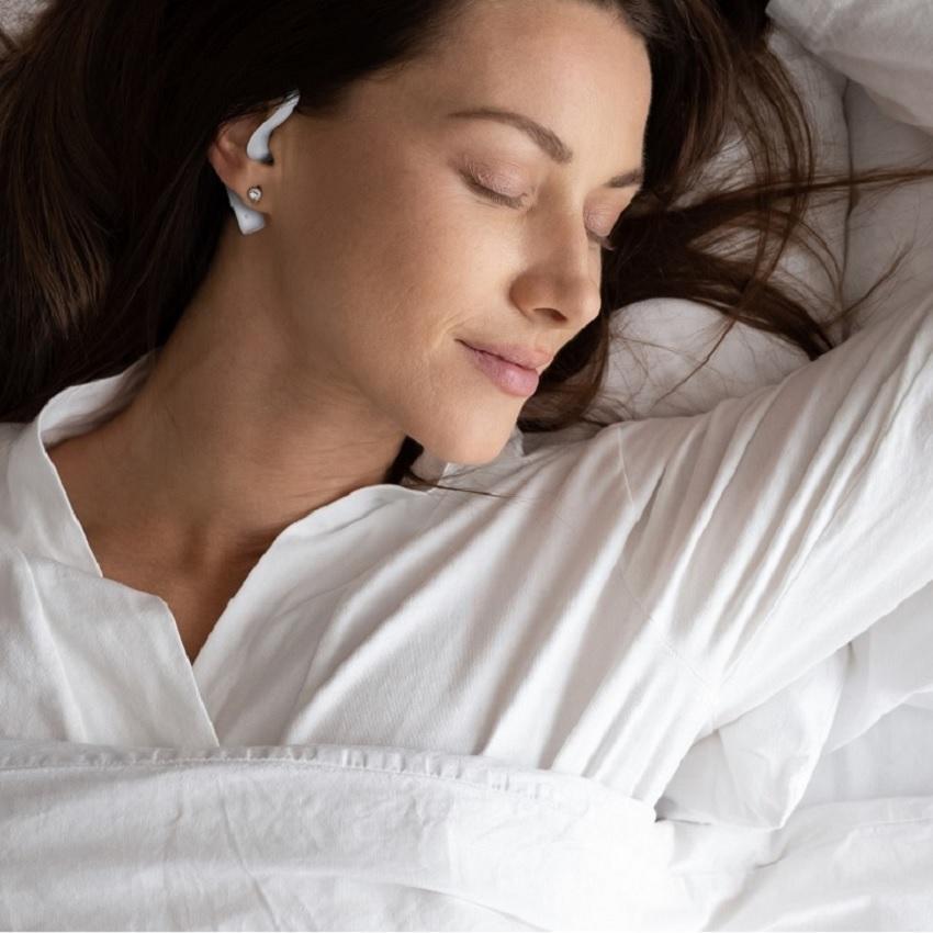 A young sleeping brunette woman enjoys a happy sleep as she wears her soundoff sleep earbuds