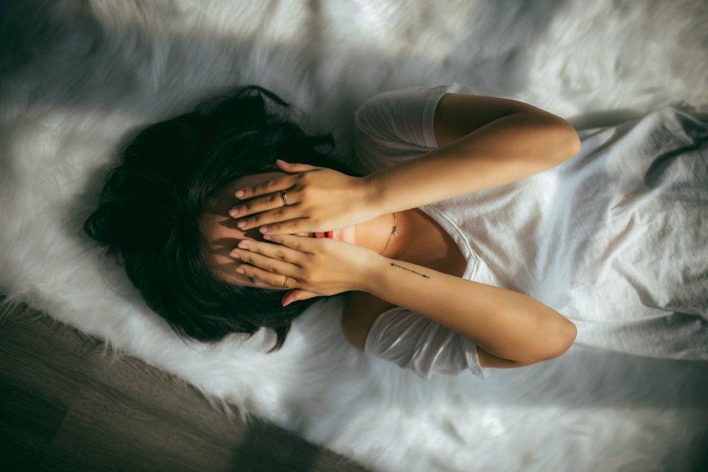 Woman in bed covering face with hands