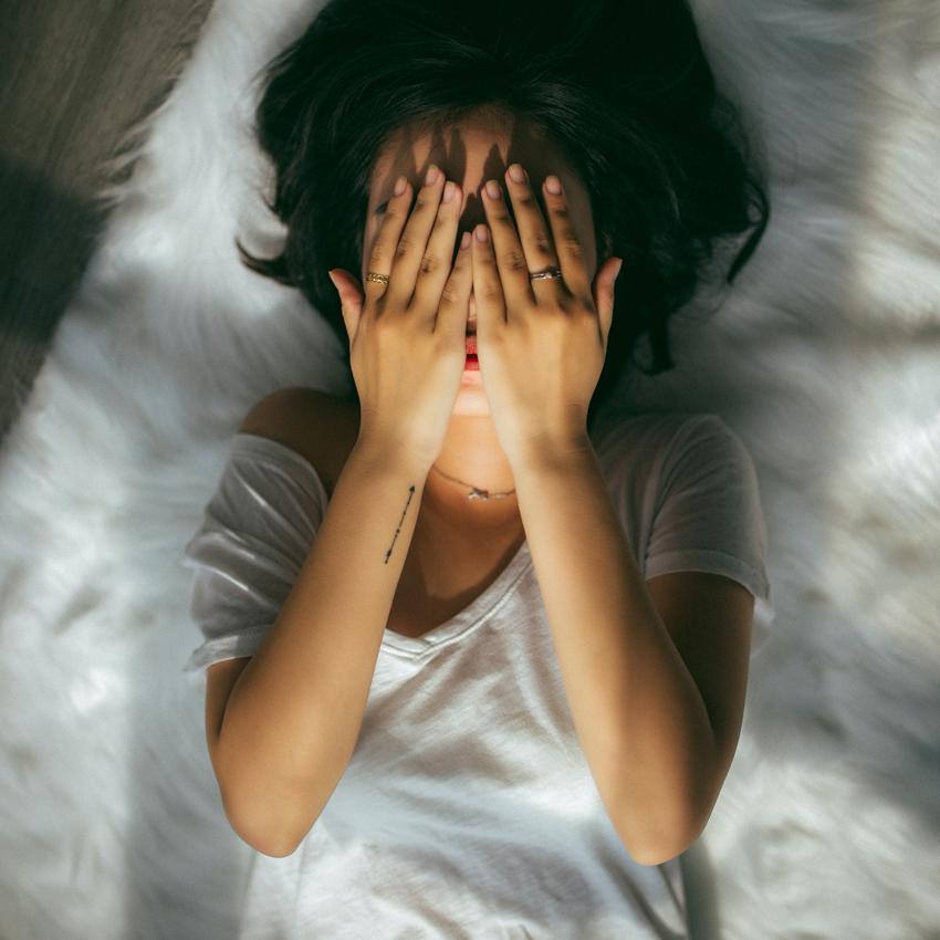 A woman lying in bed, covers her face in frustration because she can't sleep.