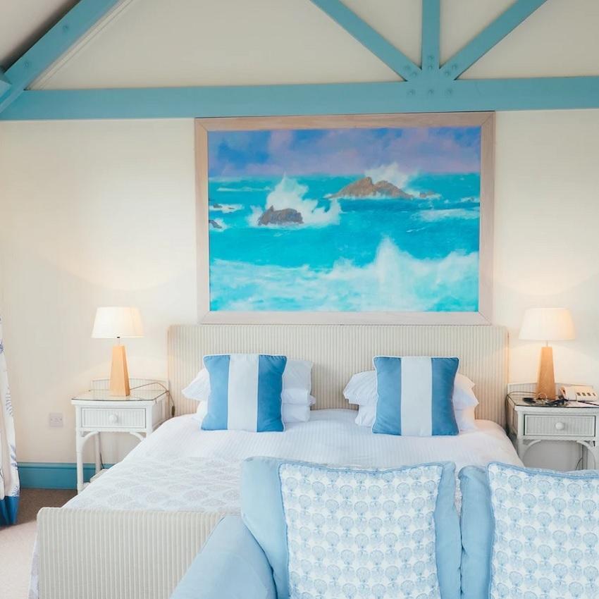 A bedroom painted and decorated in soothing shades of blue with a seascape painting above the bed.