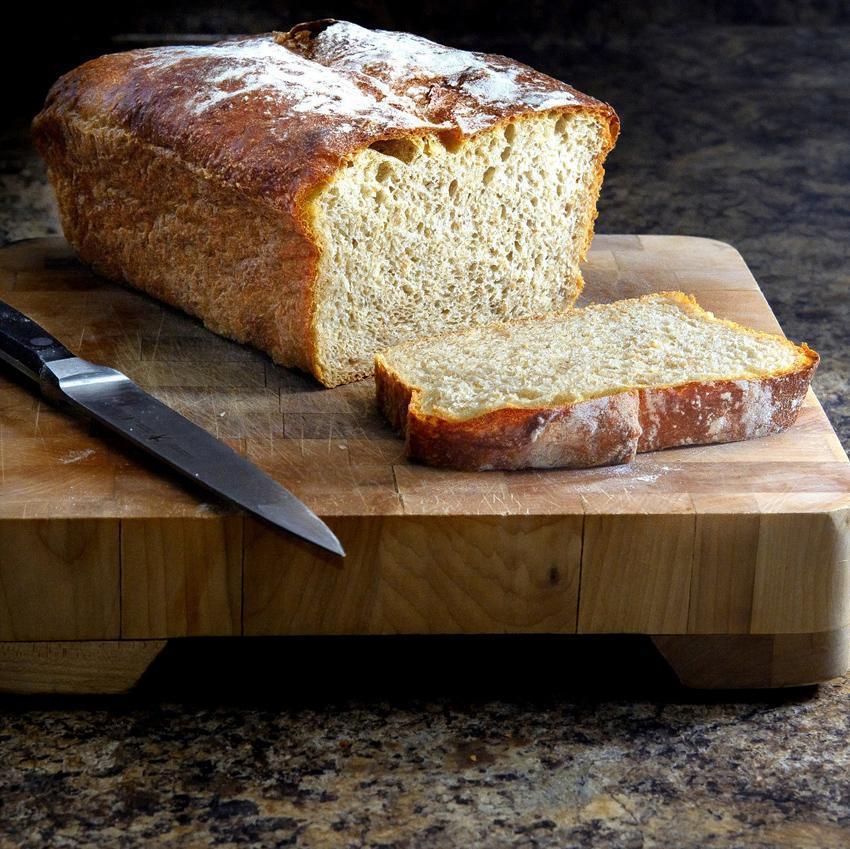 A fresh loaf of wholegrain bread rests on a butcher block cutting board with a knife and one slice already cut. Whole grains are a good source of Vitamin B6.