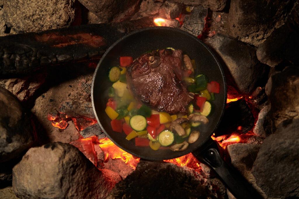 A one pan meal of meat and colorful sleep-supporting vegetables over the hot coals of a campfire