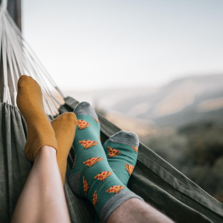 Two pair of socked feet side-by-side in a hammock overlooking a mountain view.