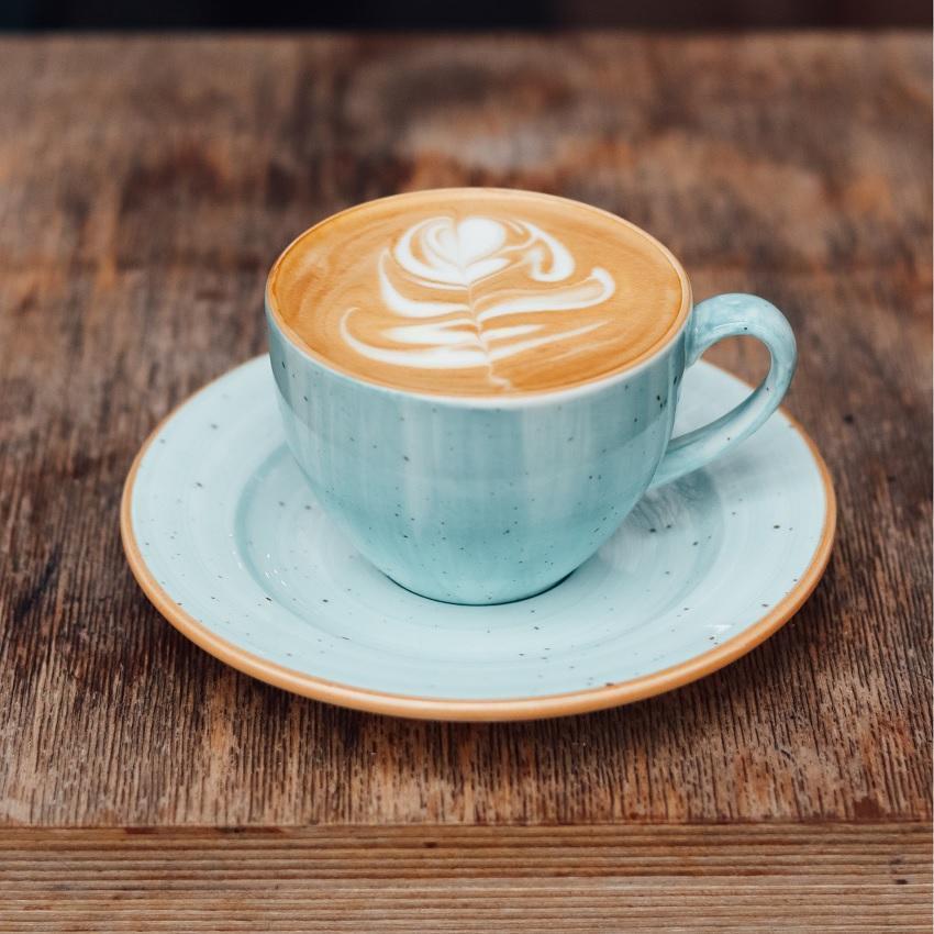 A foamy latte in a pale blue mug and saucer. Coffee enhances focus--but so do naps--and naps have an added benefit: they boost memory consolidation.