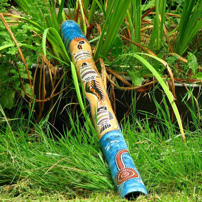 A colorfully-painted instrument called a didgeridoo laying in the grass.