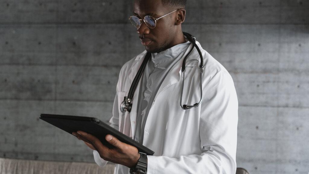 A male doctor wearing a stethoscope and holding an iPad, reviews patient information.