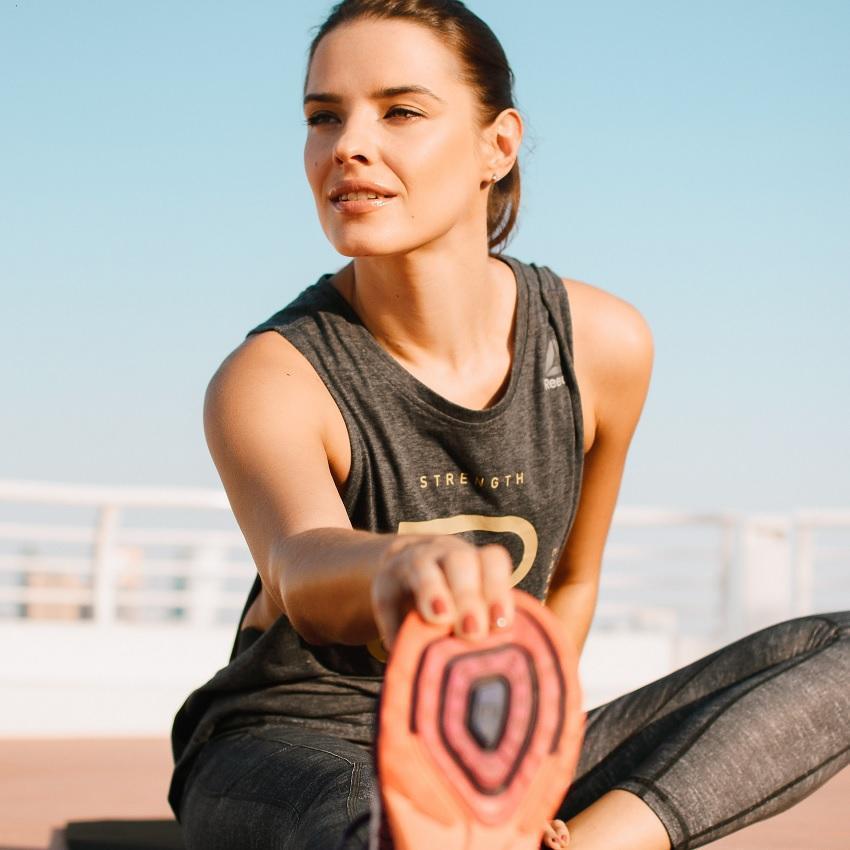 A fit young woman, does seated leg stretches before heading out for a run.