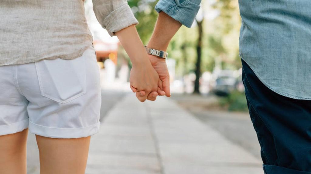 Close up on joined hands as a man and woman stroll down the street