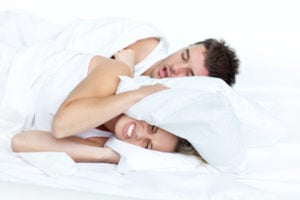 Woman grimacing with pillow over her head while husband snores
