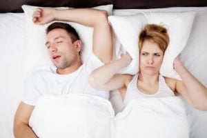 Woman with pillow pushed up around her ears because husband is snoring