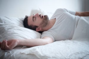 Man sleeping on his back in white bed, mouth open snoring