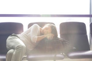 A young woman stretched across airport seats sleeping on travel bag