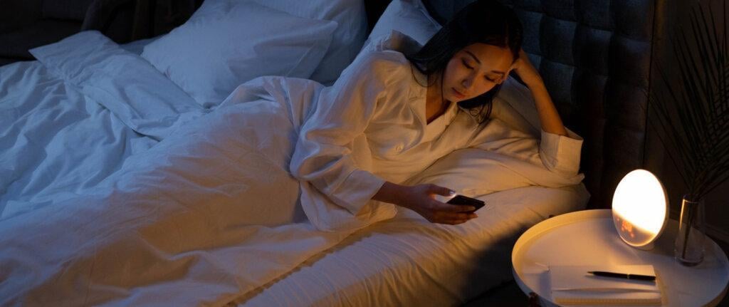A woman in bed, awake in the night, using cell phone.