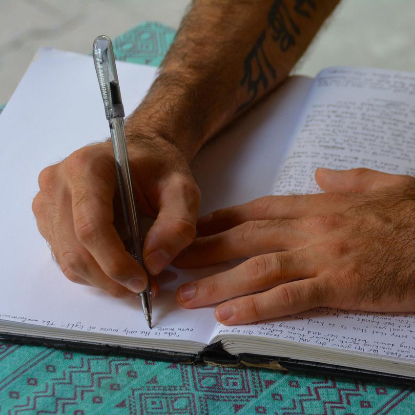 Photo of a man's hands, writing in a journal.