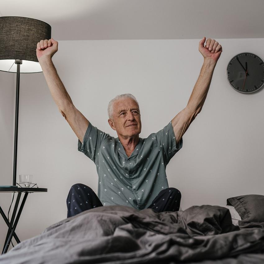 Man sitting up in bed  in the morning and stretching his arms up