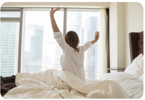 lady sitting up in bed stretching in the morning with sunlight coming through window