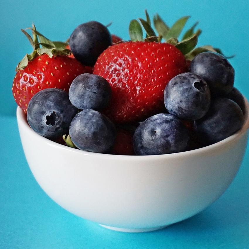 A white bowl filled with luscious-looking blueberries and strawberries, on a bright blue background.