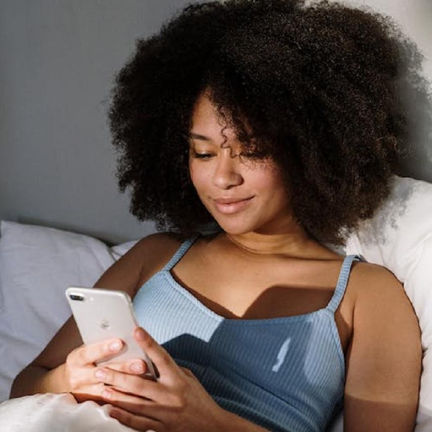 A young woman in bed viewing her cell phone. One of the most obvious reasons you're awake is that you take your phone to bed.