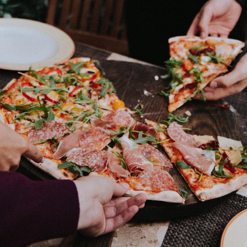Hands reaching in to grab slices of a pizza pie. Spending more time socializing and less time on social media, helps you relax and fall asleep easier.