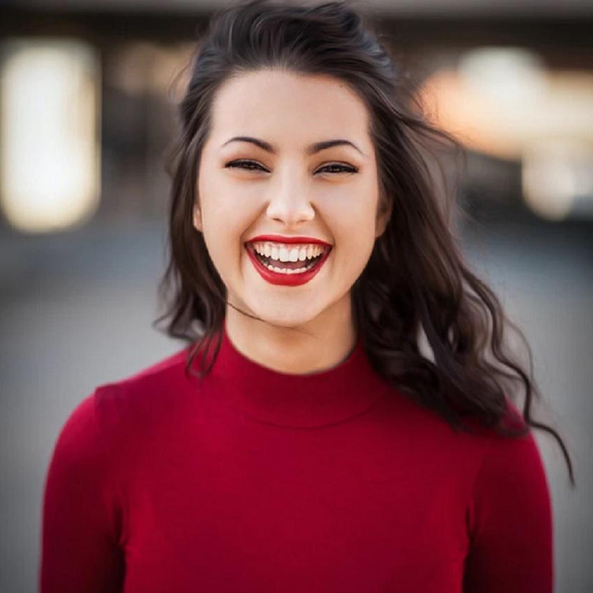 Close up of a happy, attractive young woman in a red sweater and red lipstick, smiling broadly.