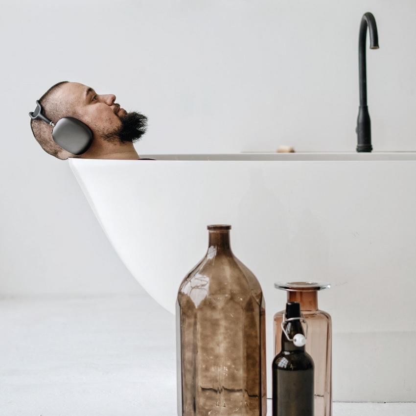 Man in bathtub with headphones on. 3 Decorative bottles next to bathtub