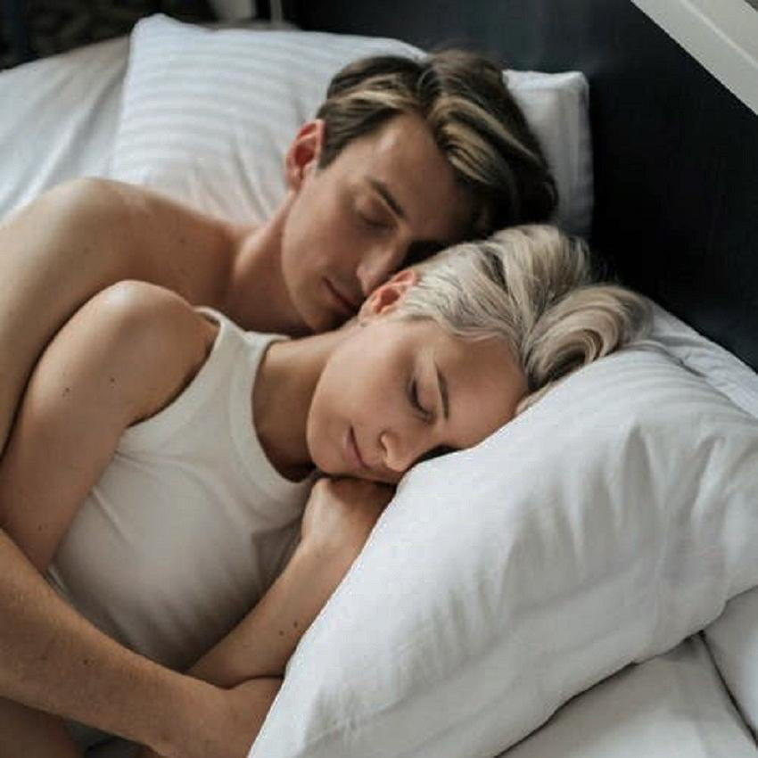 A young couple snuggles in bed fast asleep.