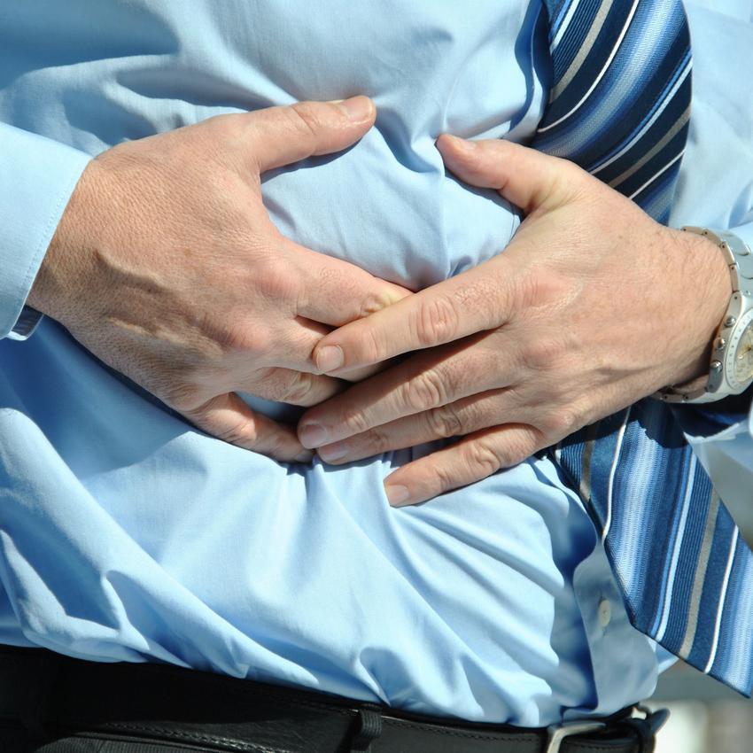 A man grips his stomach with both hands. Digestive health is important for a good night's sleep.