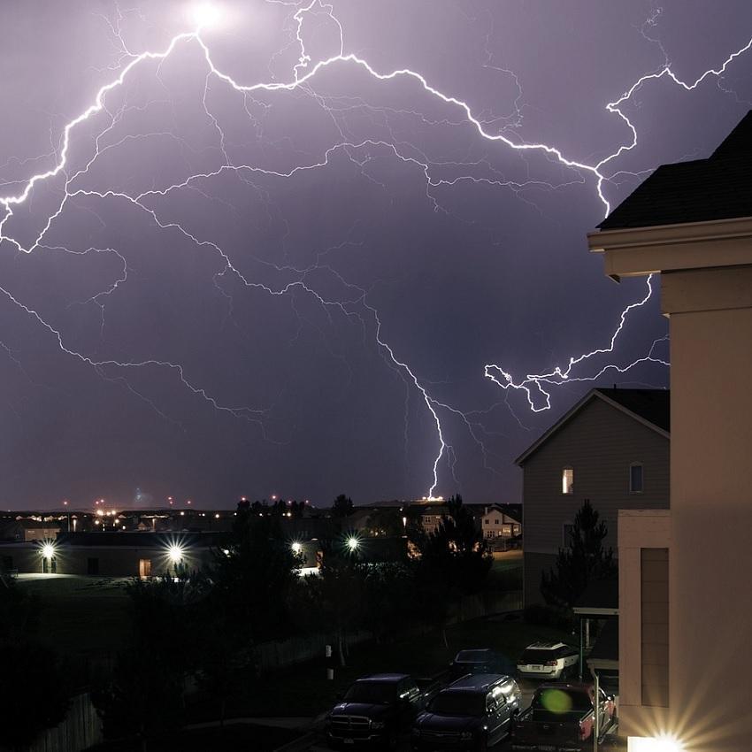 Lightning lights up a night sky over a neighborhood--representing thunderstorm noises that can prevent peaceful sleep.