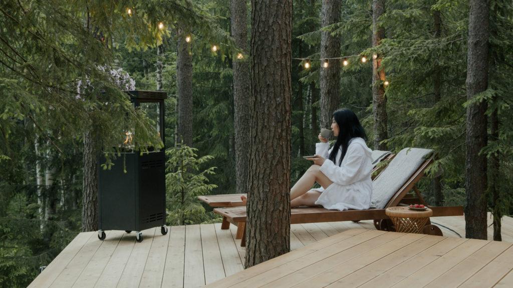 Lady sitting on deck on woods drinking tea.