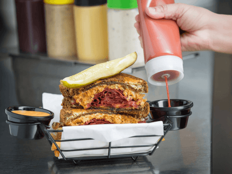 Squeezing sauce onto condiment cup next to a corned beef sandwich