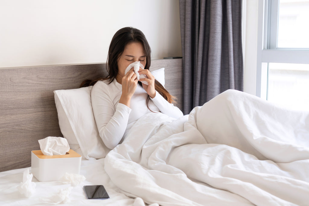 Woman lying in bed blowing her nose with a tissue.