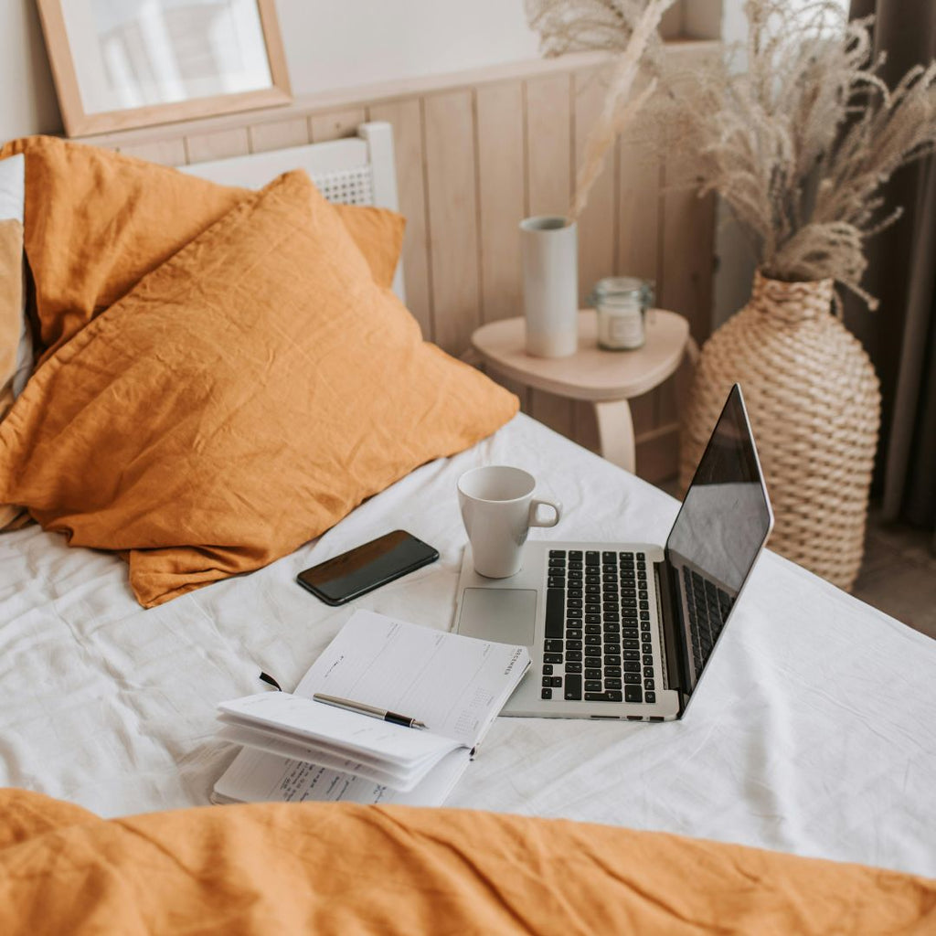 a bed with laptop, cup, phone and notebooks