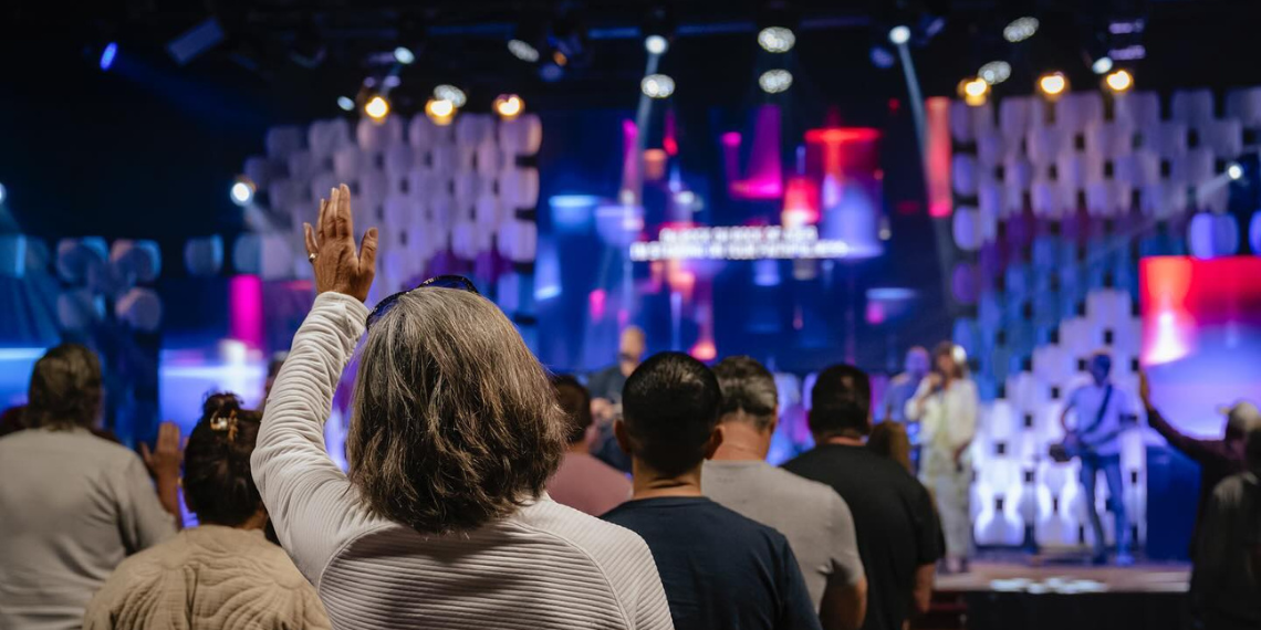 Woman Praising at Capistrano Beach Church: A heartfelt moment captured as a woman raises her hand in worship during a service, expressing her devotion and spirituality.