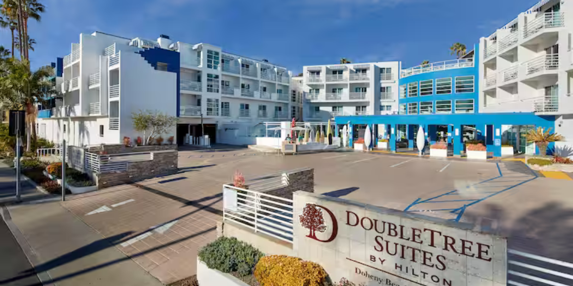 Daytime view of the exterior of DoubleTree Suites by Hilton Hotel Doheny Beach, a modern and inviting hotel building surrounded by lush landscaping, under a clear sky.