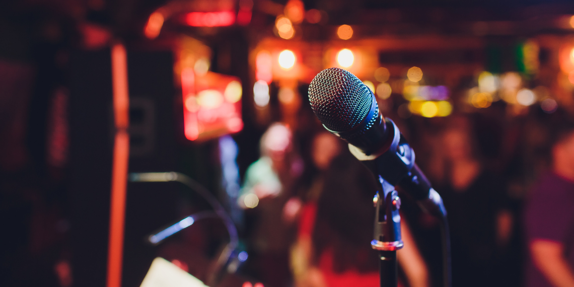 A microphone stands prominently at The Coach House, poised for live music performances, as the bar sign gleams in the background, signaling an evening filled with entertainment and lively atmosphere.