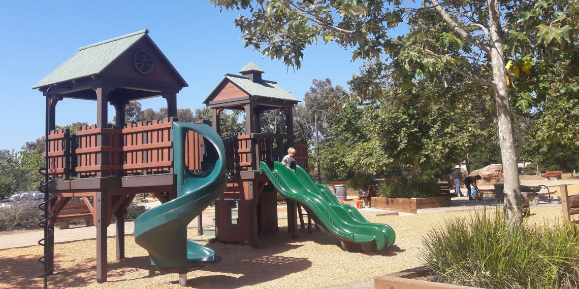 A vibrant playset at Los Rios Park, featuring slides, swings, and climbing structures, surrounded by lush greenery.