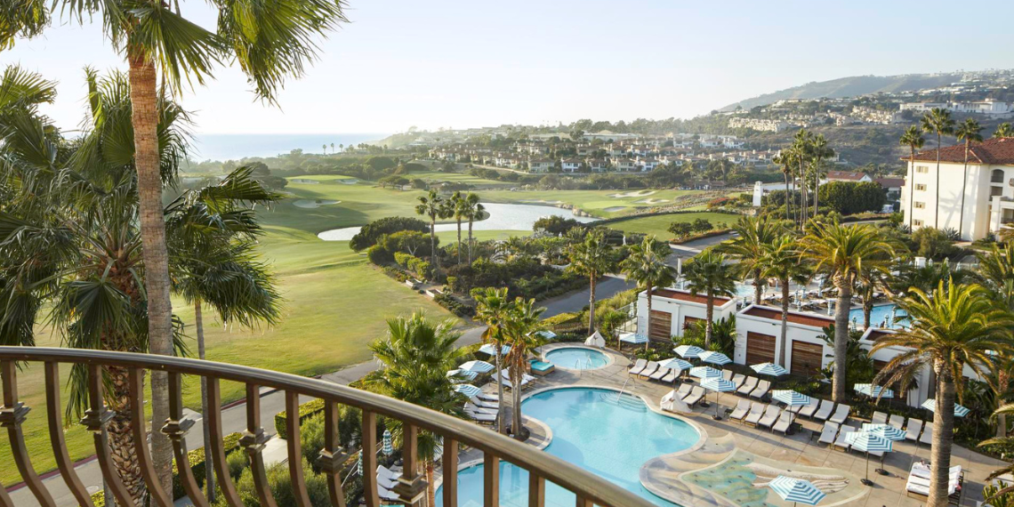 Scenic balcony view from Monarch Beach Resort, capturing the lush green golf course, inviting pool, and the expansive ocean beyond, providing a picturesque blend of natural beauty and leisure.