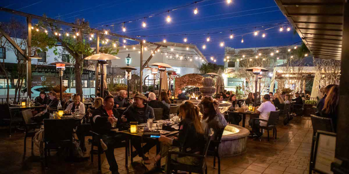 Night scene at Trevors by the tracks in San Juan Capistrano, with people dining outdoors under warm lighting, enjoying dinner and drinks amidst a lively atmosphere.