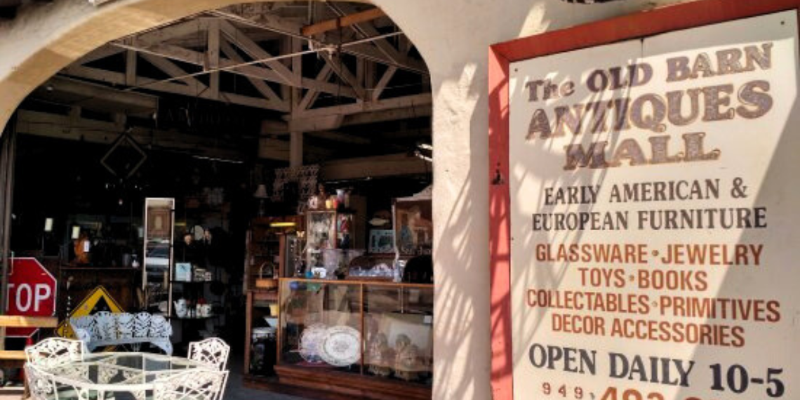 A rustic, weathered barn facade featuring the Old Barn Antique Mall sign in San Juan Capistrano, evoking a nostalgic charm and inviting visitors to explore vintage treasures within.