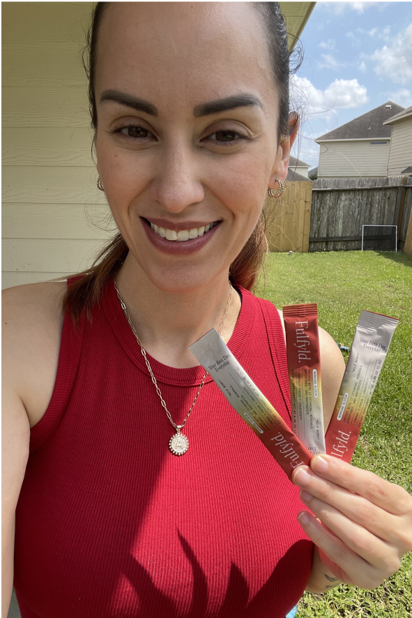 Woman holding three packets of drink mix in a backyard.