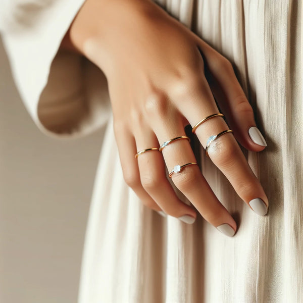 Close-up view of a woman's hand featuring minimalist gold rings and bangles on a soft neutral background, emphasizing the simple elegance of the jewelry
