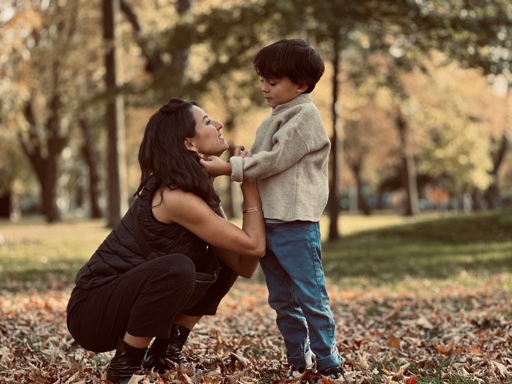 Mother affectionately looking up at her young son as they stand among autumn leaves in a park, capturing a tender family moment