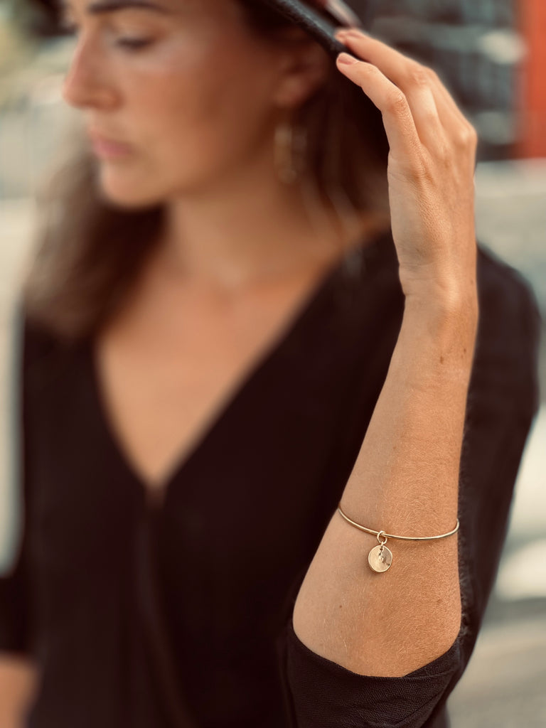 Elegant woman in a black outfit adjusting her hat, showcasing a delicate 14k gold bracelet with a charm, handmade by What If You Stayed in Montreal