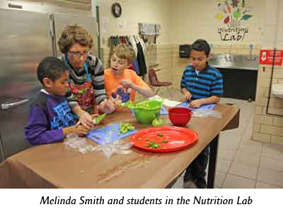 Three young students with their teacher in a kitchen at a wood table.